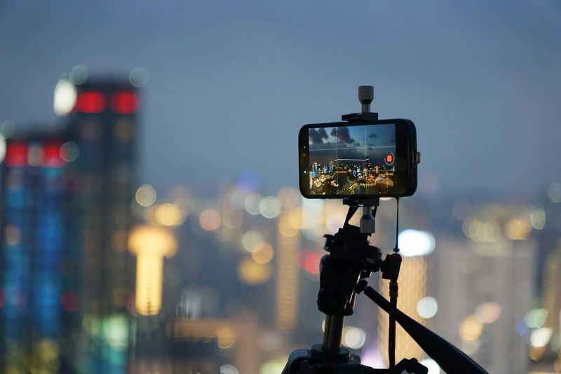 Ein Smartphone auf einem Stativ filmt nachts die Skyline einer Stadt