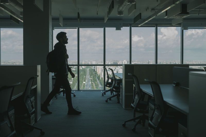 An office worker walking past large windows with a view of the city